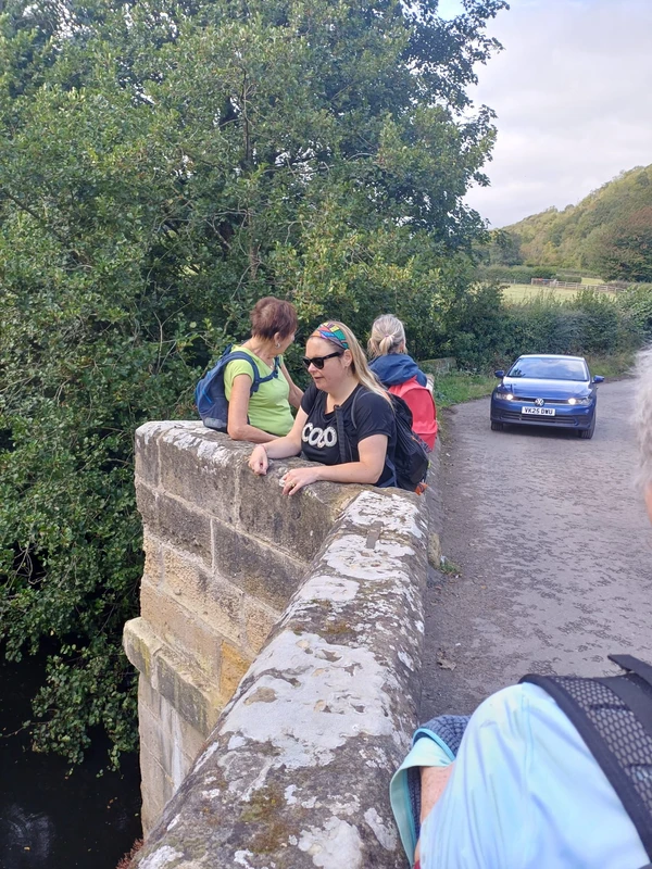 A few of the group stand by a wall on a concrete and stone bridge with a car a few metres away,
probably waiting to get past