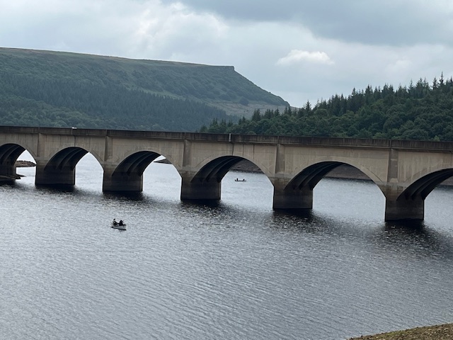 Two small boats can barely be seen either side of a bridge spanning the reservoir