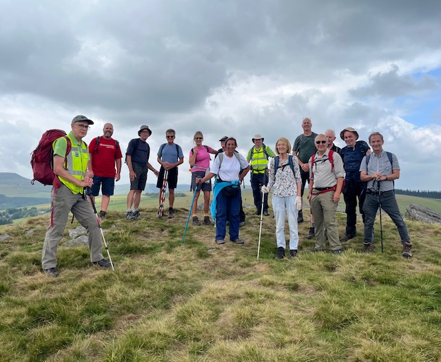 The group assemble at the top of a hill under a cloudy sky for a photo